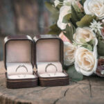 A pair of wedding rings is placed in a jewelry box and a bouquet of flowers is placed on the side.