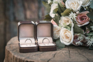 A pair of wedding rings is placed in a jewelry box and a bouquet of flowers is placed on the side.