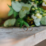 Wedding rings on a wooden stand against the background of the bride's bouquet