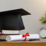 Mortar board with degree paper and books on wood table. graduation concept.