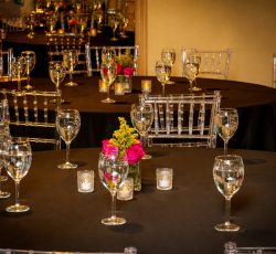 Round tables with black tablecloths, clear chairs, wine glasses, candles, and small floral centerpieces.