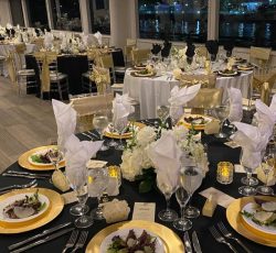 Elegant banquet hall set with round tables, gold accents, plated salads, and folded white napkins, overlooking water.